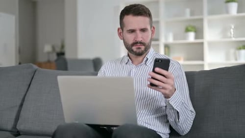Young Man Using Laptop and Smartphone at Home