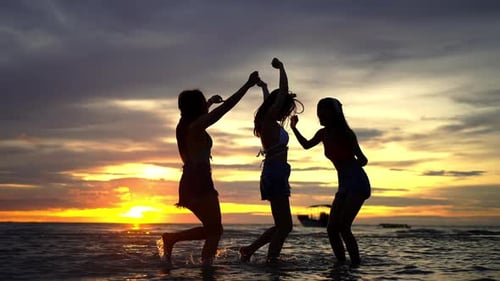 4K Silhouette Group of Asian woman friends playing together on the beach at summer sunset.