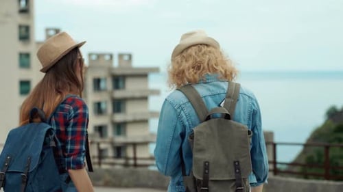 Back View of Two Pretty Girls Young Women Friends Travelers Walking Outdoors