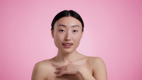 Young Attractive Wellgroomed Asian Woman Touching Her Neckline Enjoying Condition of Her Skin Pink