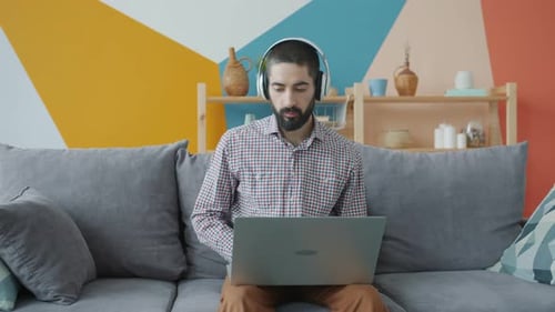 Man Using Laptop and Headphones on Couch Indoors