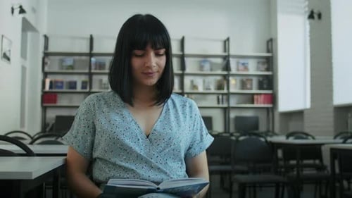 Happy Woman Reads a Book in the Library Chooses Books From the Shelf
