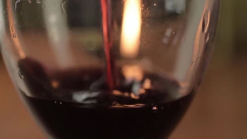 Pouring red wine into a glass with warm candle background close up