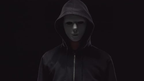 Hooded Figure in Blank Mask Stands in Darkness