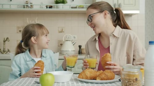 Mère et fille prenant leur petit déjeuner en mangeant des croissants et des verres à jus de fruits à la maison
