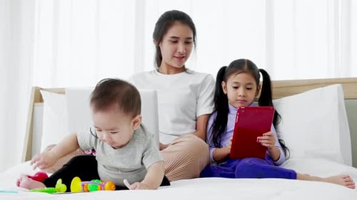 Mother and Children Play on Bed with Devices