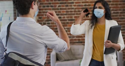 Man and woman wearing face masks greeting each other by touching their elbows at office