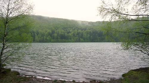 Rätselhafter einsamer Mann, der auf einer Bank am Seeufer im Bergwald sitzt.