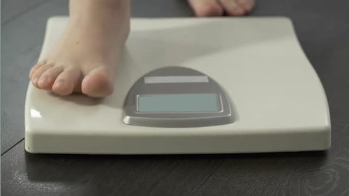Frau tritt auf Waage, um Ergebnisse der Gewichtskontrolle zu sehen, gesunde Ernährung