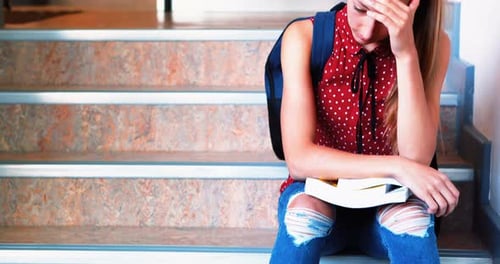 Sad schoolgirl sitting alone on staircase