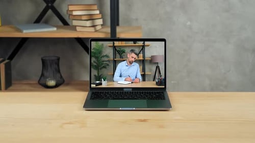 Laptop Displaying Man Writing in Notebook on Video Call
