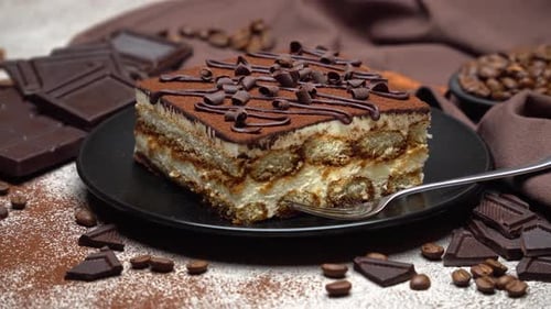 Portion of Traditional Italian Tiramisu dessert and pieces of chocolate bar