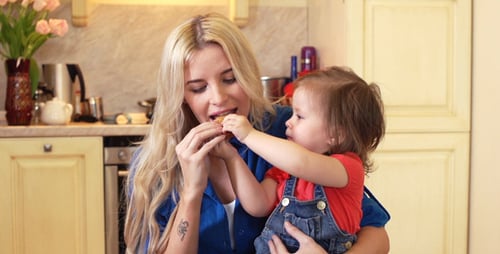 Woman Giving Cookie to Toddler in Kitchen
