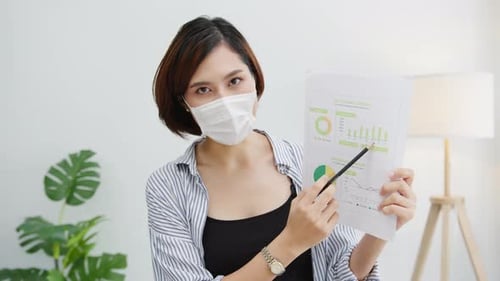 Asian business woman wear face mask presentation to colleague about plan in video call in office.