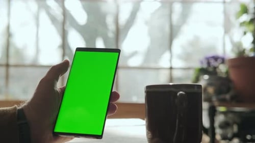 A Male Hand Holds a Phone with a Mockup Green Screen and Drinks Coffee
