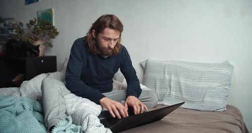 Man Works on Laptop While Sitting on Bed