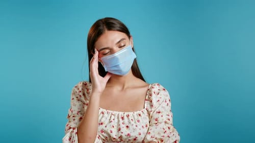 Young Tired Woman in Protective Mask Is Dissatisfied, Unhappy. Blue Studio Portrait of Girl, She Is