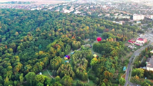 Beautiful sunbeams illuminate the balloons that fly over the park, green trees.