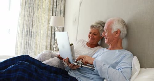 Senior Couple Relaxing in Bed with Laptop