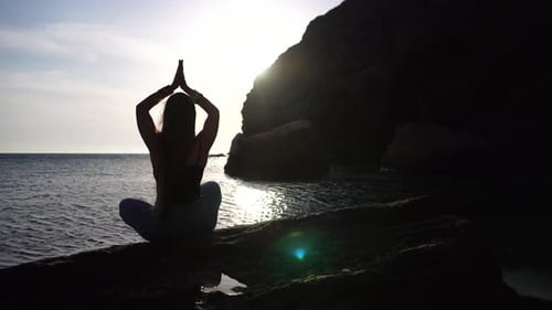 Jeune femme aux cheveux longs pratiquant des étirements en plein air sur un tapis de yoga au bord de la mer sur un coucher de soleil chaud