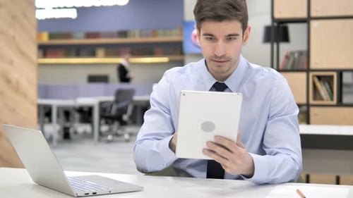 Young Adult Man Celebrating Success Using Tablet in Office