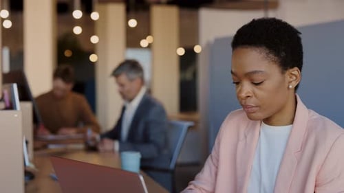 Young Black Businesswoman with Laptop Computer and Papers Working at Cozy Office