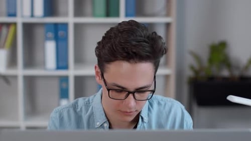 Young Confident Focused Guy Wearing Eyeglassesworking Online on Computer Reading and Typing at