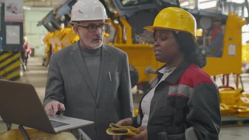 Female Factory Worker and Engineer Using Laptop and Talking