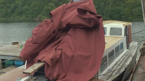 Man Covers Boat with Canvas Near Tree Lined Lake