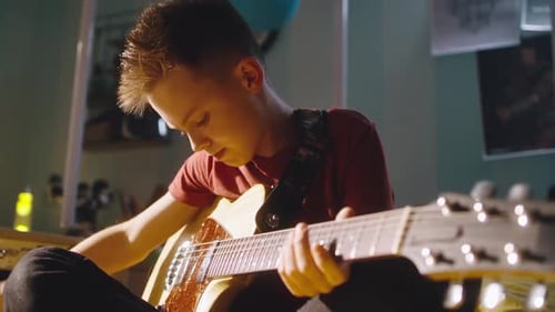 Boy Plays Electric Guitar in Warmly Lit Room