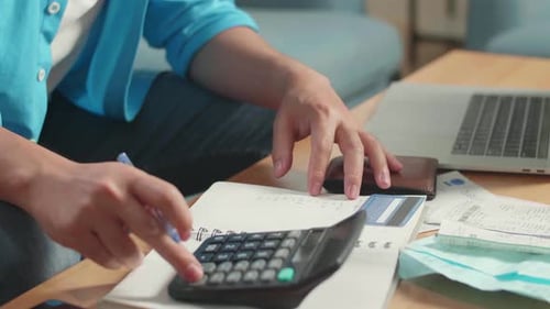 Person Calculates Home Finances, Writes in Notebook