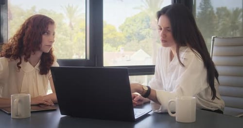 Dos mujeres en una reunión de negocios, trabajando con un portátil en la oficina.