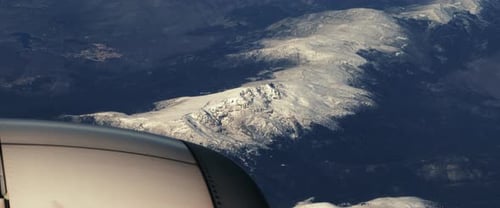 Das Flugzeug fliegt über die verschneiten Berggipfel. Blick durch ein Flugzeugfenster