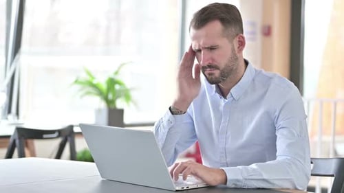 Young Man with Laptop Having Headache in Office