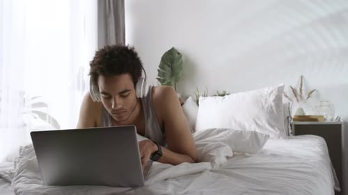 Man With Laptop Listening to Headphones on Bed