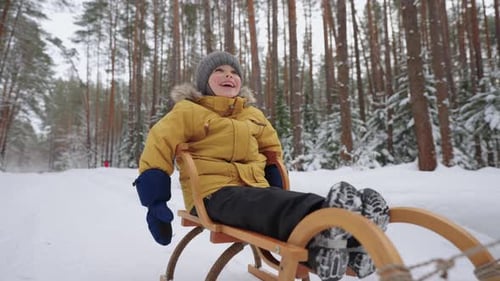 Porträt eines lächelnden Jungen 34 Jahre alt in Zeitlupe, der im Winter auf einem Schlitten in einem verschneiten Wald fährt
