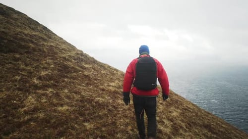 Hiker Walking Along Grass Slope To Misty Sea