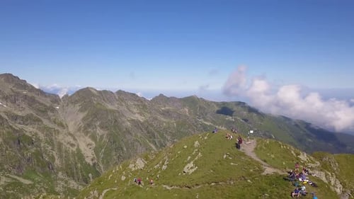 Ascending aerial view of hilltop with hikers sitting on ground enjoying the view from the mountain p