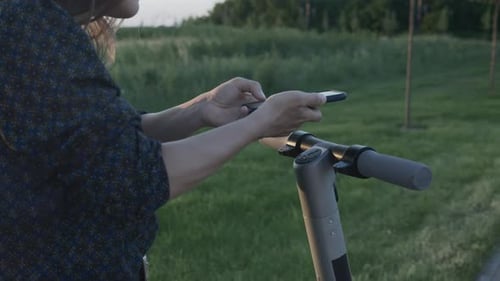 Woman Stands by Electric Scooter with Mobile Phone