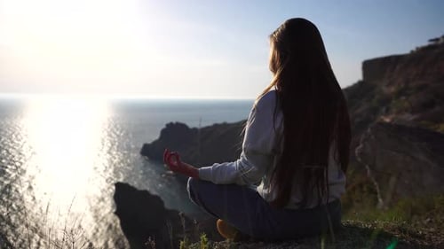 Junge Frau mit langen Haaren übt Stretching im Freien auf einer Yogamatte am Meer bei warmem Sonnenuntergang