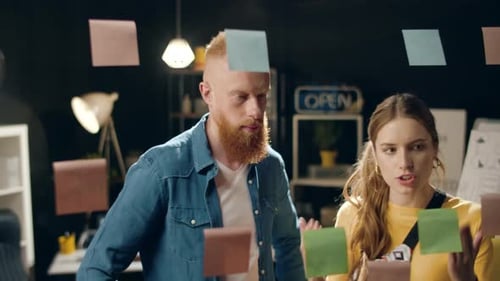 Un couple d'affaires en gros plan discute d'un projet près d'une planche de verre dans un bureau de nuit.