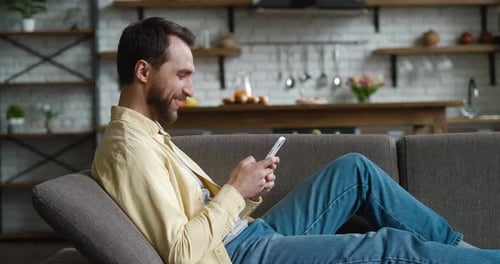 Man Relaxing on Couch Using Mobile Phone
