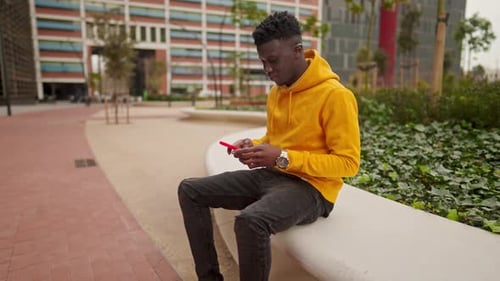 Afroamerikanischer Mann in einem Stadtzentrum im Chat mit Handy