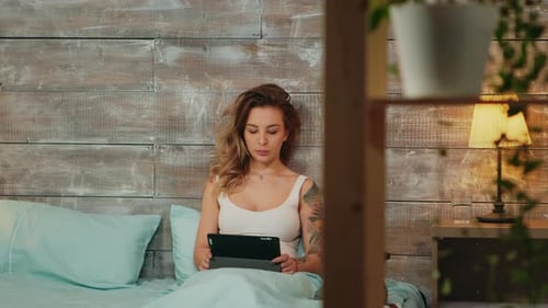 Woman Relaxes in Bed with Tablet and Dog