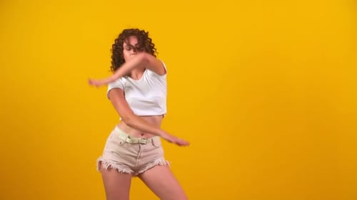 Energetic Young Woman Dancing on Yellow Background