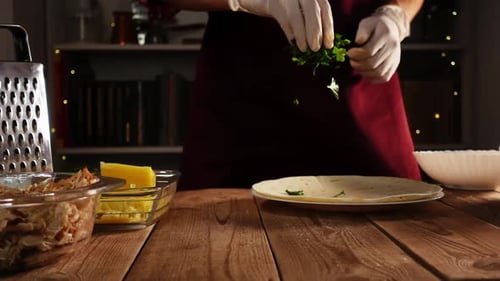 Young Caucasian Chef with Gloved Hands Sprinkles Greenery on Pita for Cook Mexican Enchilada