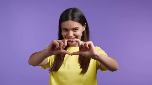 Young Woman Makes Heart Shape with Hands and Smiles