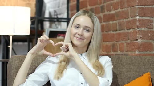 Woman Makes Heart Shape With Hands on Sofa