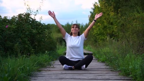 Young Attractive Fit Girl Sit on Wooden Bridge in Lotus Pose and Say Hello To the Sun with Smile in
