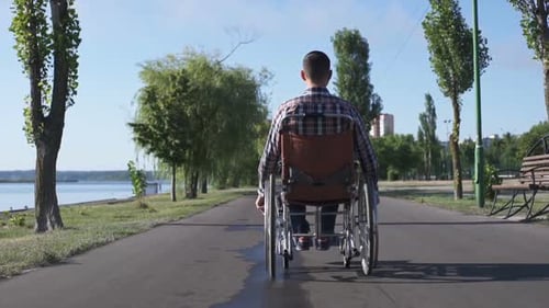 Man in Wheelchair Moving Along Waterfront Path